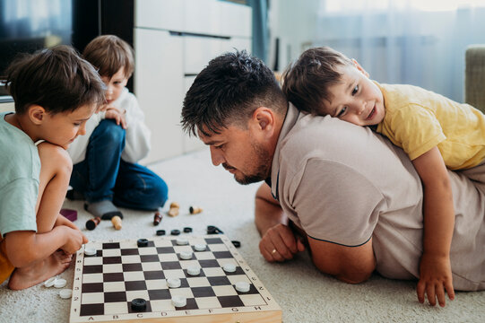 Father spending leisure time playing checkers with kids at home