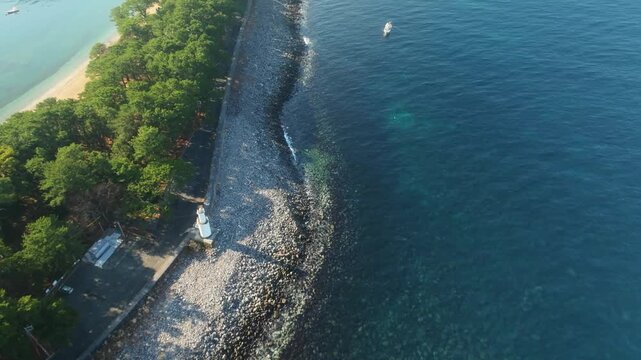 Aerial view of the lighthouse, coastal rocks, and lush green trees meeting the deep blue sea at Mihama Cape Park, Numazu, Shizuoka, Japan.