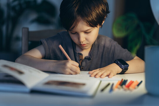 Boy doing homework at home in the evening with art supplies on the desk