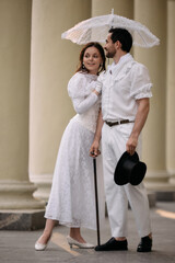 Smiling couple in historical costumes standing close under lace umbrella. Concept of book covers,...
