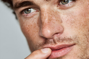 Obraz premium Young man applying lip balm onto his lips on light grey background, closeup