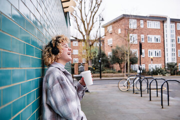 Cheerful woman laughing while having coffee on footpath