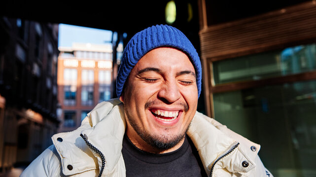 Young man wearing knit hat laughing during sunny day