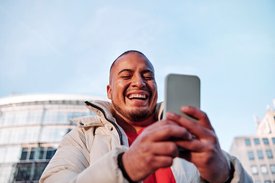 Cheerful man using smart phone during sunny day