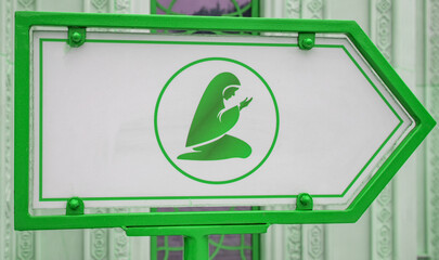 A sign indicating the place of prayer and depicting a Muslim woman, against the backdrop of a mosque wall