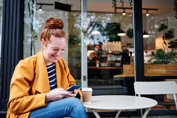 Smiling woman using smart phone while sitting at cafe