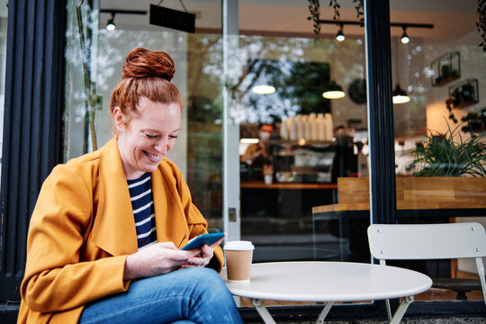 Smiling woman using smart phone while sitting at cafe