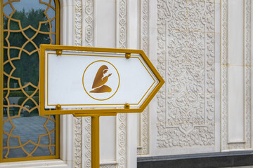 A sign indicating the place of prayer and depicting a Muslim woman, against the backdrop of a mosque wall