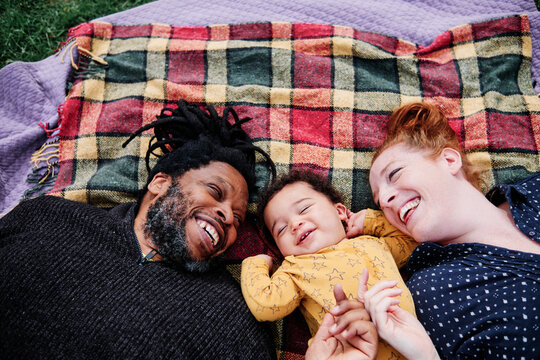 Happy family playing with cute son while lying on picnic blanket at park