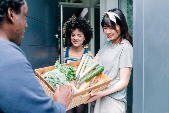 Delivery man giving fresh vegetable basket to women at doorway