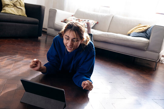 Happy woman cheering and using tablet PC at home