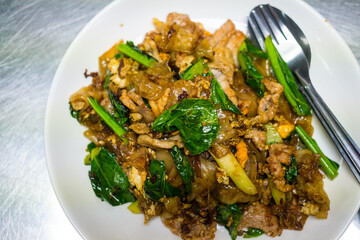 Fried wide noodles with soy sauce kale and egg served on white dish.