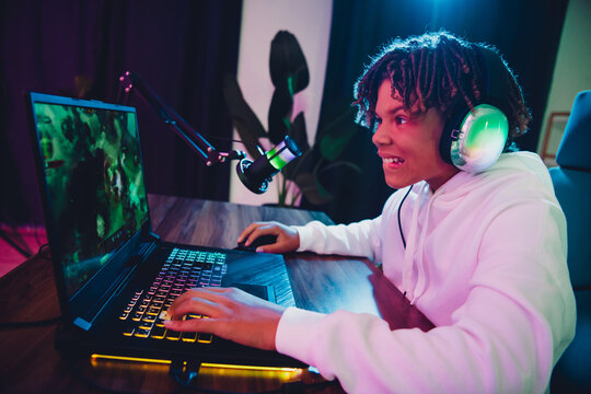 Energetic Young Gamer Engaged in Online Streaming with Headset and Laptop in a Stylish Neon-Lit Indoor Setup - Powered by Adobe