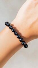 Elegant Wrist Adornment: A close-up showcases a wrist elegantly adorned with a string of lustrous, black beads. Simple, yet striking, the photo highlights the minimalist beauty of the bracelet.