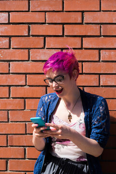 Amazed young woman with dyed hair looking at her cell phone