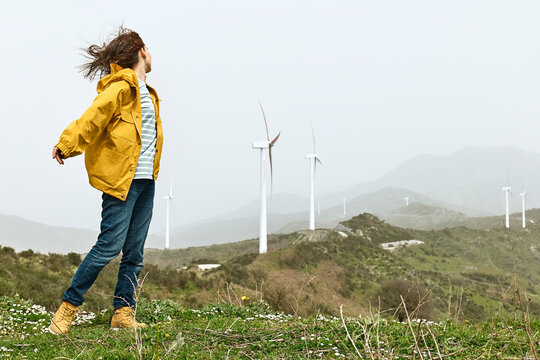 Woman standing near wind turbines on mountain under sky