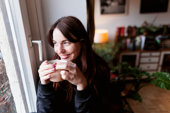 Brunette woman drinking tea by the window