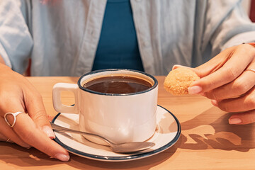 Woman enjoying a relaxing moment at a cafe, and a small cookie with a cup of rich black coffee,...