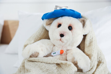 Pediatrics concept. Toy bear with ice bag and thermometer in bed