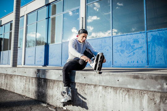 Young man sitting on ramp putting on inline skates