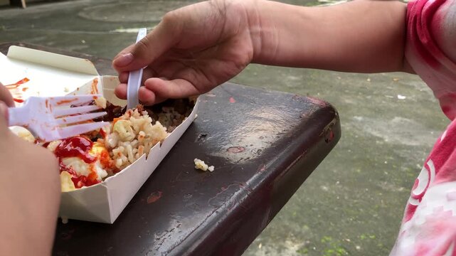 young girl with a chubby figure is eating lunch, which consists of rice and a deep-fried chicken leg.