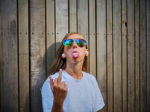 Girl wearing sunglasses and showing middle finger in front of wooden wall
