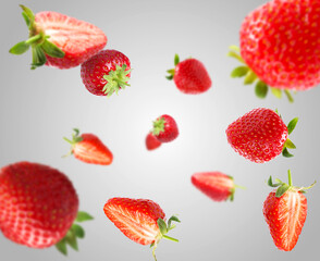 Yummy fresh strawberries swirling in air against grey background