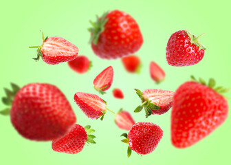 Yummy fresh strawberries swirling in air against green background