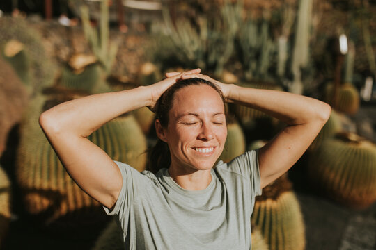 Happy woman with hands behind head in cactus garden