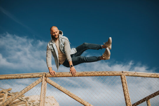 Man jumping over fence under sky