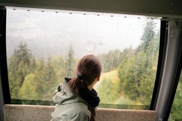 Switzerland, Valais, woman in a cable car looking out of rainy window