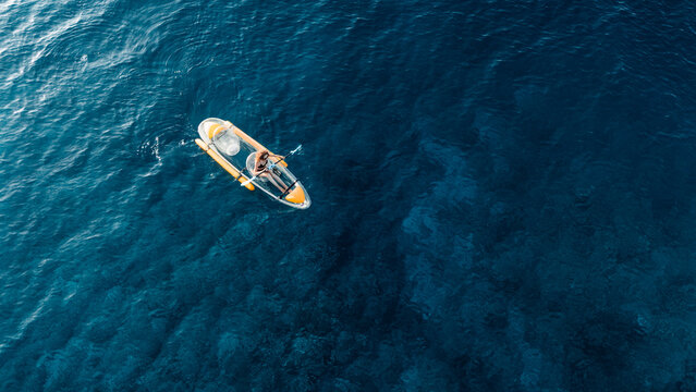 Woman swims on transparent plastic kayak in summer blue sea. Drone view, top down