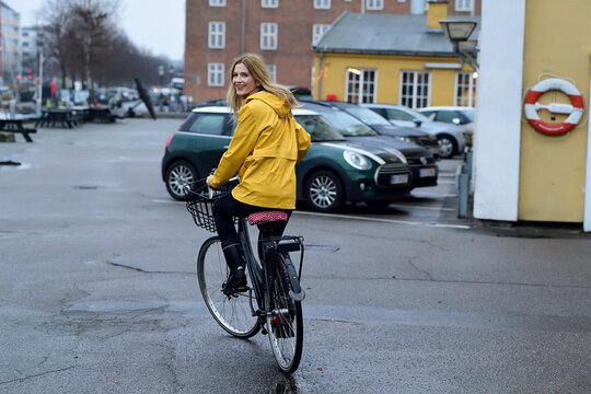 Denmark, Copenhagen, happy woman riding bicycle on waterfront promenade in rainy weather