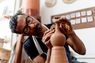 Close-up of male artist making earthenware while sitting in workshop