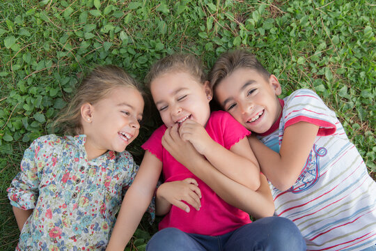 Portrait of three laughing children lying side by side on a meadow