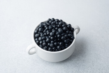 Blueberries in white bowl on light background for breakfast, diet or wellness concept