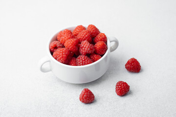 Bowl of fresh raspberries with scattered berries for snack or breakfast concept