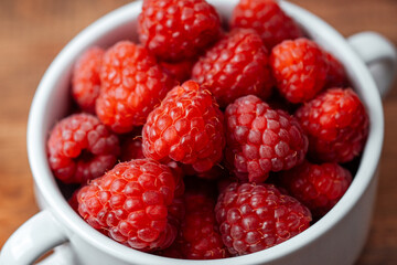 Raspberries in white bowl. on wooden table for rustic food styling or organic eating concept