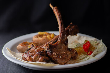 Rack of lamb with vegetables on a white plate on a black background