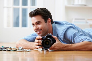 Happy male photographer lying on floor, holding DSLR camera, near jewelry, casual style, bright interior.