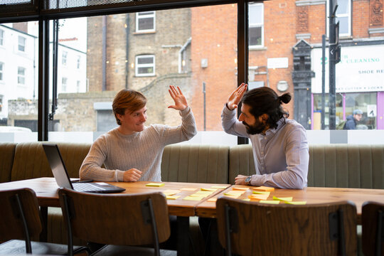 Male coworkers giving high five to each other while sitting at desk in office