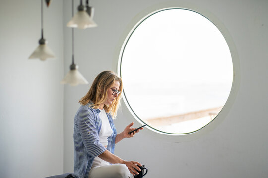 Businesswoman using smart phone sitting at window