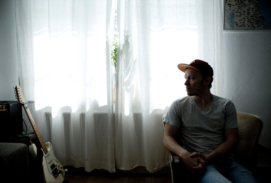 Man sitting in front of window, looking at his guitar