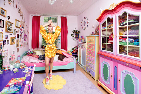 Young woman with hand raised sticking out tongue standing in flashy bedroom