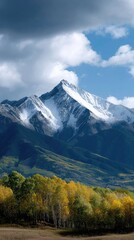 Fototapeta premium Breathtaking mountain range features snow-covered summits, lush forests, and autumn colors under a moody sky in a tranquil landscape