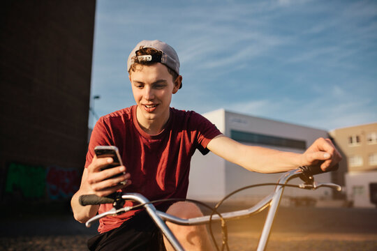 Young man with BMX bicycle looking on cell phone