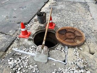 Open manhole cover on the street, orange barriers, road repair. Accident with a sewer manhole in the city. Concept of sewerage, underground communications