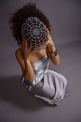 Vertical shot of young adult multiethnic woman sitting on floor wearing metallic dress, beaded...