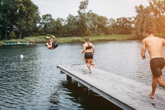 Sportive people running on jetty, jumping into lake after workout training