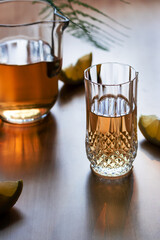Iced tea in a crystal glass, carafe and lemons on a marble table at golden hour